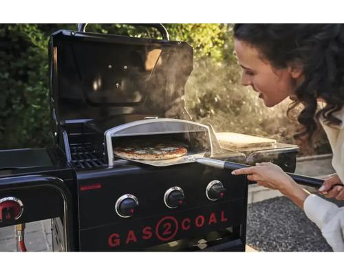 Femeie introduce pizza cu o paletă într-un grătar pe gaz cu accesoriu pentru cuptor de pizza