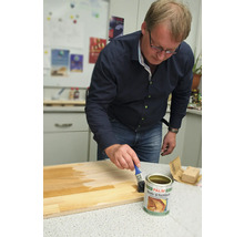 Un bărbat aplică lac pentru bărci și iahturi pe o scândură de lemn