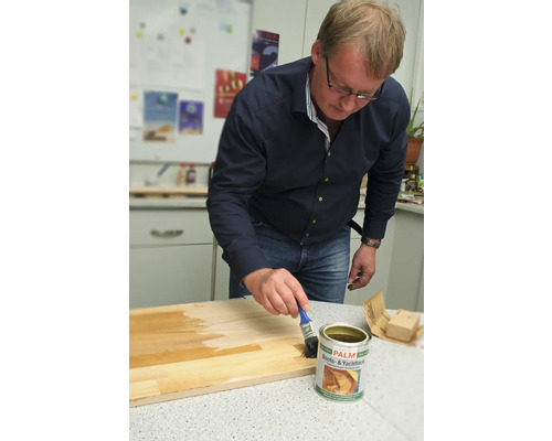 Un bărbat aplică lac pentru bărci și iahturi pe o scândură de lemn