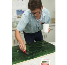 Un bărbat baituiește o scândură de lemn cu o pensulă și bait de lemn