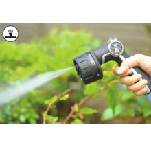 Mână ținând pistolul de pulverizare al furtunului de grădină în timp ce udă plantele