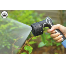 O mână ține un pistol de pulverizare pentru grădină care pulverizează apă