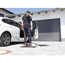 Un bărbat aspiră o preș de podea în fața unei mașini cu un aspirator fără fir.