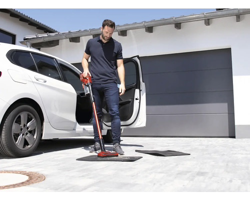 Un bărbat aspiră o preș de podea în fața unei mașini cu un aspirator fără fir.