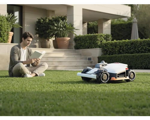 Un bărbat citește o carte în grădină lângă robotul de tuns iarba.