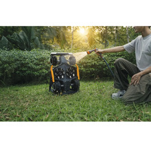 Bărbat curăță un robot de tuns iarba cu un furtun de apă în grădină.