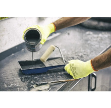 O persoană toarnă vopsea într-o cuvă de vopsea lângă o rolă de vopsea și o spatulă