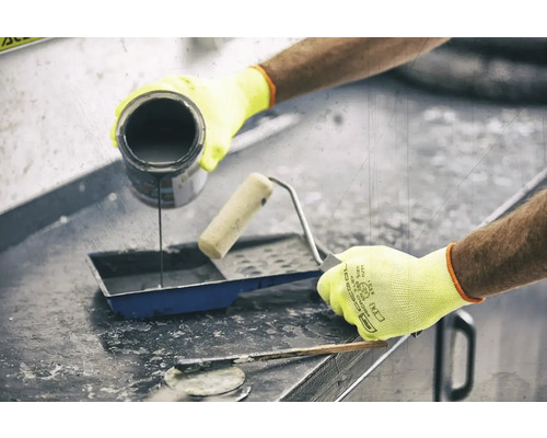 O persoană toarnă vopsea într-o cuvă de vopsea lângă o rolă de vopsea și o spatulă