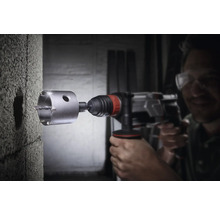 Un bărbat găurește un perete de beton cu o carotă.