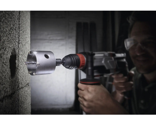 Un bărbat găurește un perete de beton cu o carotă.