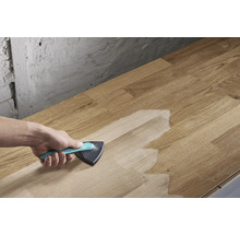 O persoană aplică un tratament de suprafață cu o pensulă triunghiulară pe o scândură de lemn.