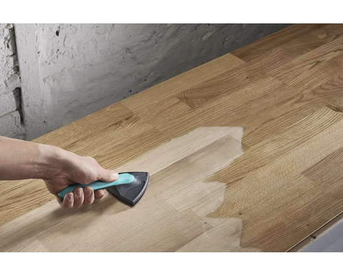 O persoană aplică un tratament de suprafață cu o pensulă triunghiulară pe o scândură de lemn.