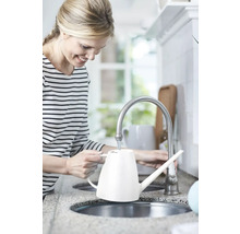 Femeie umplând o stropitoare albă la robinetul din bucătărie.