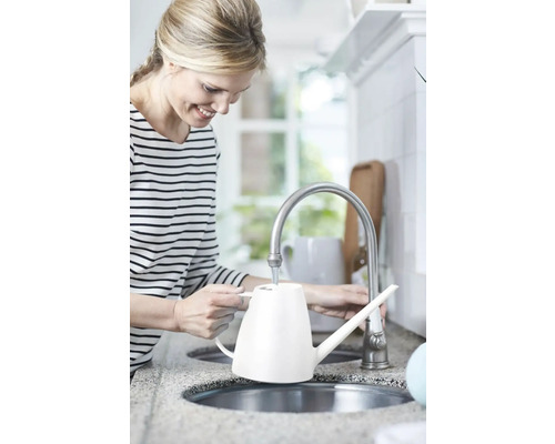 Femeie umplând o stropitoare albă la robinetul din bucătărie.