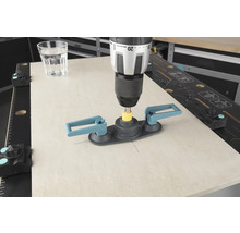 O mașină de găurit cu ajutor pentru găurirea plăcilor de faianță găurește o placă de faianță, lângă ea se află un pahar cu apă.