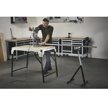 Un bărbat lucrează cu o mașină de găurit pe un banc de lucru, cu unelte și un banc de lucru în fundal.