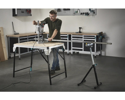 Un bărbat lucrează cu o mașină de găurit pe un banc de lucru, cu unelte și un banc de lucru în fundal.