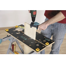 O persoană găurește o scândură de lemn cu o mașină de găurit pe un banc de lucru.