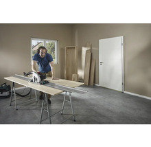 Un bărbat taie lemn cu un fierăstrău circular manual pe un banc de lucru într-o cameră.