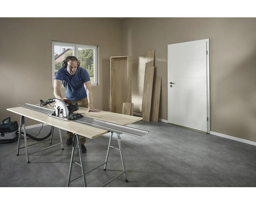 Un bărbat taie lemn cu un fierăstrău circular manual pe un banc de lucru într-o cameră.