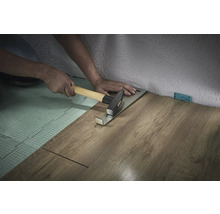 Persoană care montează laminat cu bară de tracțiune și ciocan