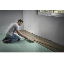 Bărbat care montează podea laminată în interior cu distanțiere