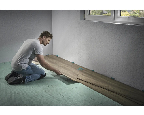 Bărbat care montează podea laminată în interior cu distanțiere