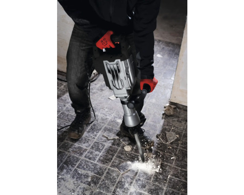 Un bărbat cu mănuși de lucru folosește un ciocan demolator pentru a îndepărta plăcile.