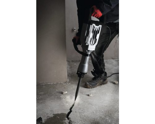 Un bărbat folosește un ciocan demolator pentru a crea o fisură într-o podea de beton.