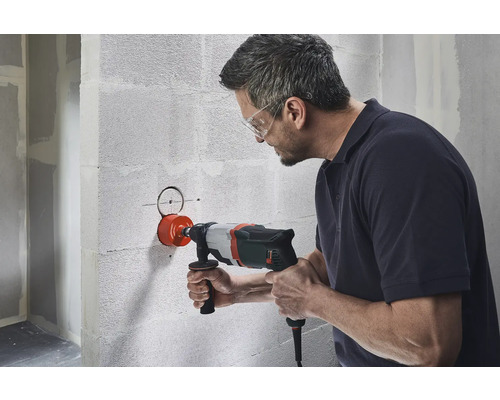 Un bărbat face o gaură într-un zid cu o carotă.