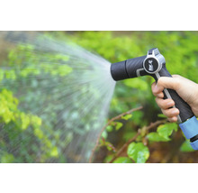 O mână ține un pulverizator de grădină care stropește plantele cu apă