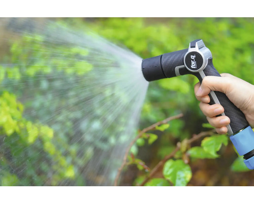 O mână ține un pulverizator de grădină care stropește plantele cu apă