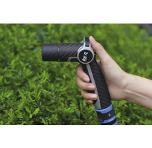 O mână ține un pistol de stropit grădina marca For Q în fața unui arbust verde