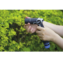 O persoană ține un pistol de stropit grădina marca for_q în fața unui tufiș verde.