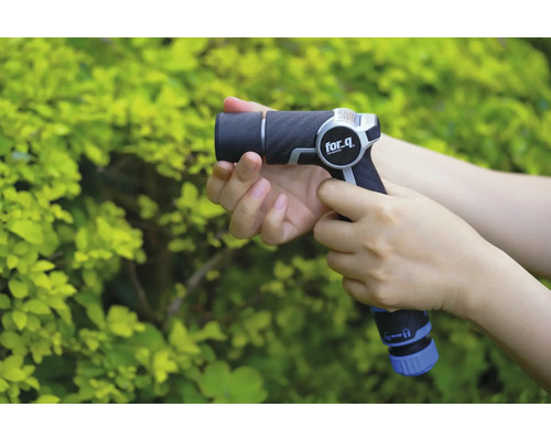 O persoană ține un pistol de stropit grădina marca for_q în fața unui tufiș verde.