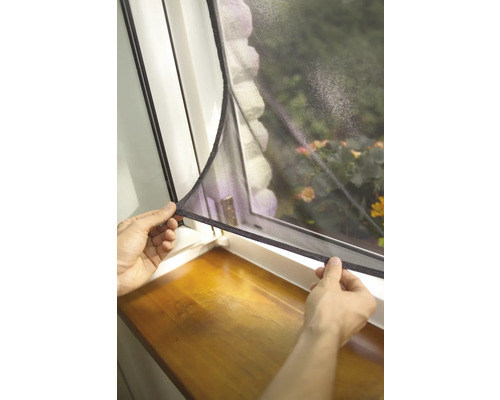 Persoană care fixează o plasă de insecte pe o fereastră.