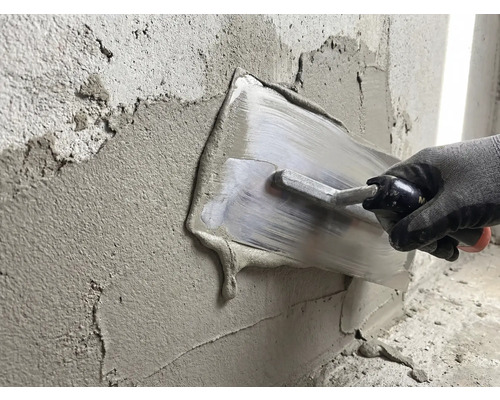 O persoană nivelează tencuiala cu o gletieră pe un perete.