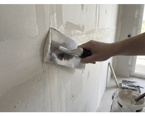 Artizan finisează peretele cu gletieră și tencuială