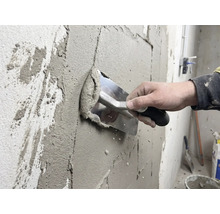 Un meșter aplică tencuială pe un perete cu o mistrie.