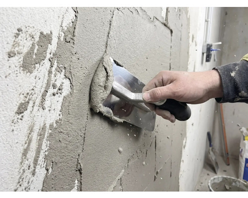 Un meșter aplică tencuială pe un perete cu o mistrie.