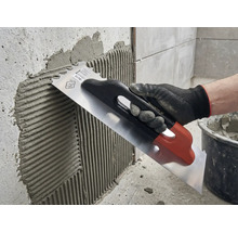 Aplicarea adezivului pentru plăci pe un perete cu o mistrie din oțel inoxidabil