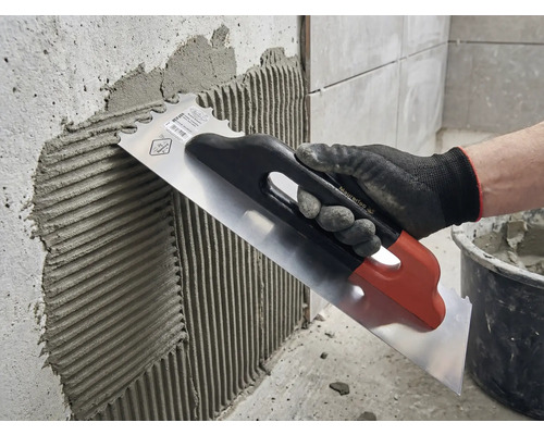 Aplicarea adezivului pentru plăci pe un perete cu o mistrie din oțel inoxidabil