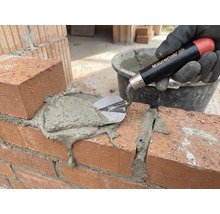 O mână cu mănușă aplică mortar pe un zid de cărămidă cu o mistrie