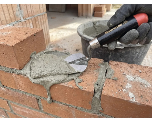 O mână cu mănușă aplică mortar pe un zid de cărămidă cu o mistrie