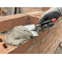 Un zidar aplică mortar pe un zid de cărămidă cu ajutorul unei mistrii.