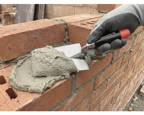 Un zidar aplică mortar pe un zid de cărămidă cu ajutorul unei mistrii.