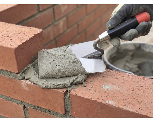 Zidar zidește cărămizi cu mistria și mortar.