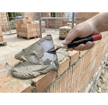 Zidar care pune cărămizi cu o mistrie și mortar.