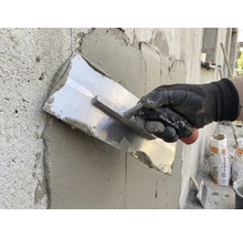 Artizan care netezește tencuiala cu o mistrie pe un perete.