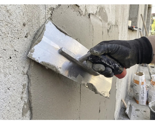 Artizan care netezește tencuiala cu o mistrie pe un perete.